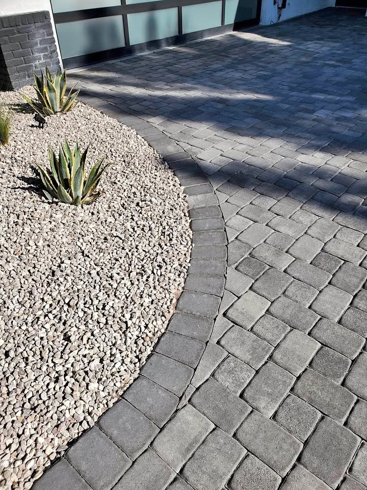 Curved stone paver driveway next to a landscaped area with small light-colored rocks and a few agave plants, expertly crafted by Paver Installation Phoenix AZ near a modern house.